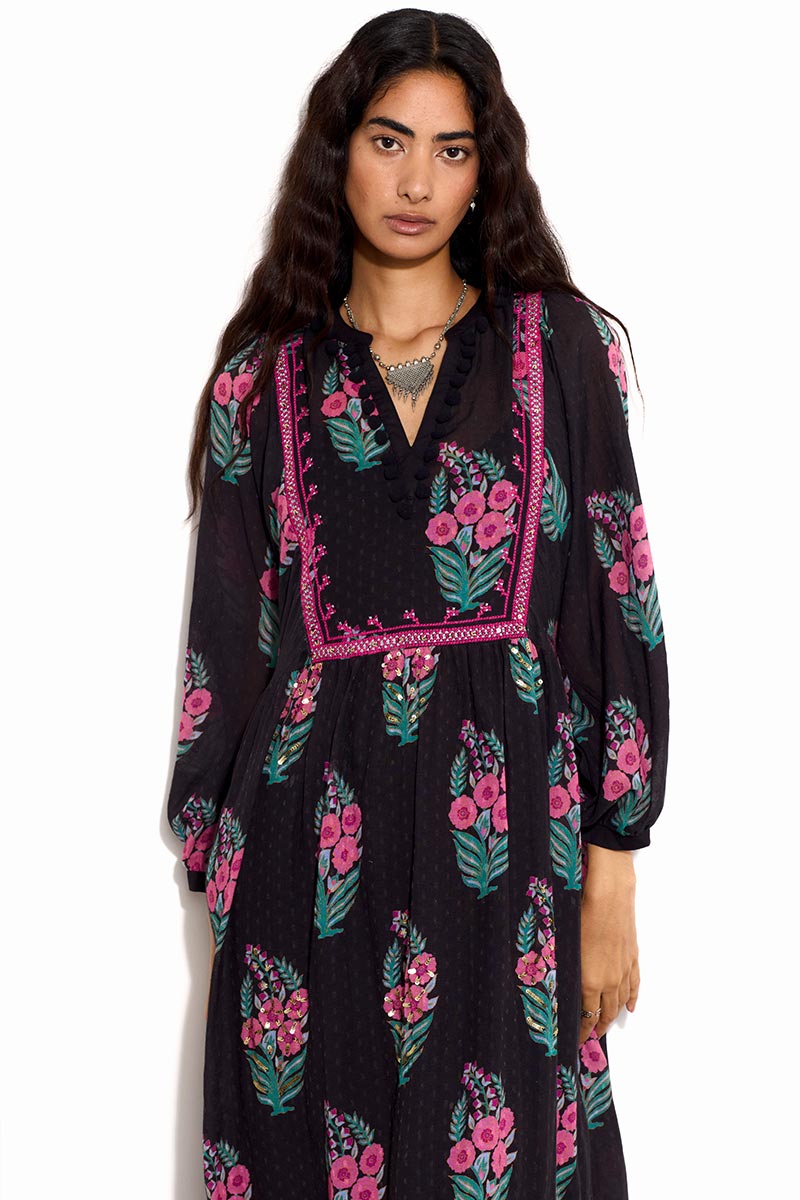 Model wears Logan black dress with pink and green spaced floral print dress. Dress has pink embroidered tapes around the front chest.