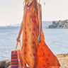 Model walks near the beach wearing East Nevaeh Sleeveless dress and carries Recycled HDPE Pink and Orange Stripe Market Bag